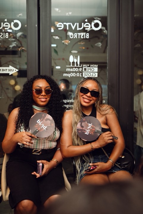 Two guests outside Oeuvre Bistro holding bund. fans